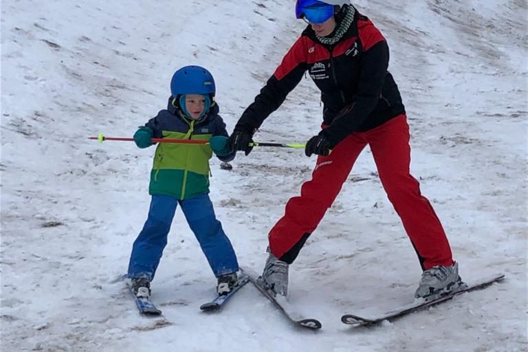 Kind lernt mit einem Lehrer das Skifahren auf einer schneebedeckten Piste.