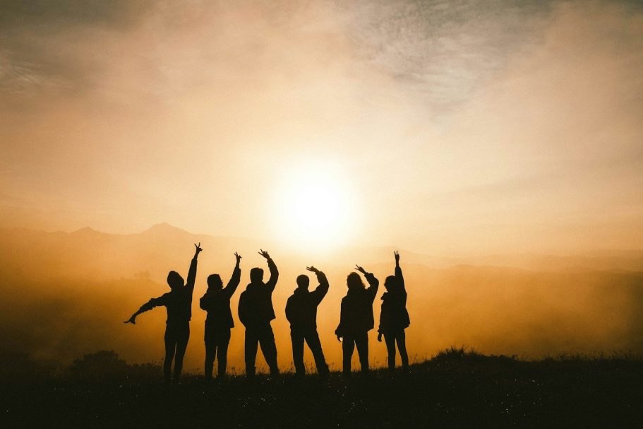 Mitglied werden Silhouetten von Menschen, die vor einem Sonnenuntergang im Nebel stehen.