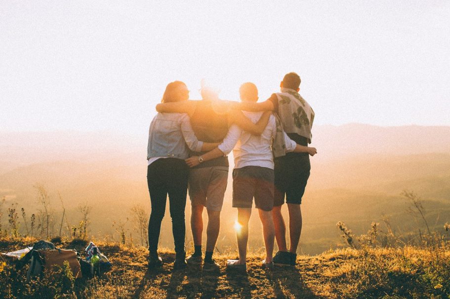 Mitglied werden Gruppe von Menschen steht umarmt bei Sonnenuntergang in einer Berglandschaft.