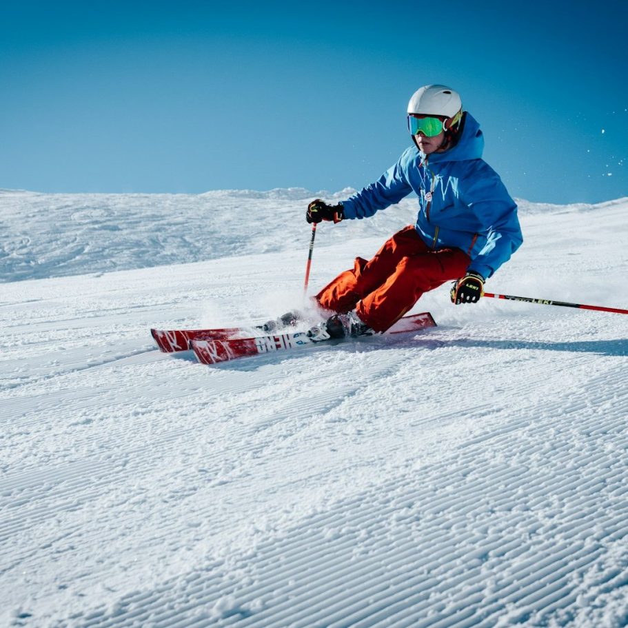 Skifahrer in blauer Jacke und roter Hose fährt über schneebedeckte Piste.